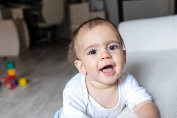A little baby boy in white bodysuit at home . Beautiful portrait of a toddler. Big-eyed baby. Remote education. Distance learninig - Fotoğraf, Görsel