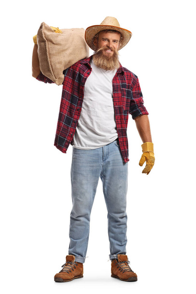 Full length portrait of a young bearded farmer carrying a sack on his shoulder isolated on white background - Фото, изображение