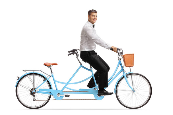 Полнометражный снимок улыбающегося жениха, катающегося на велосипеде в тандеме на белом фоне - Фото, изображение