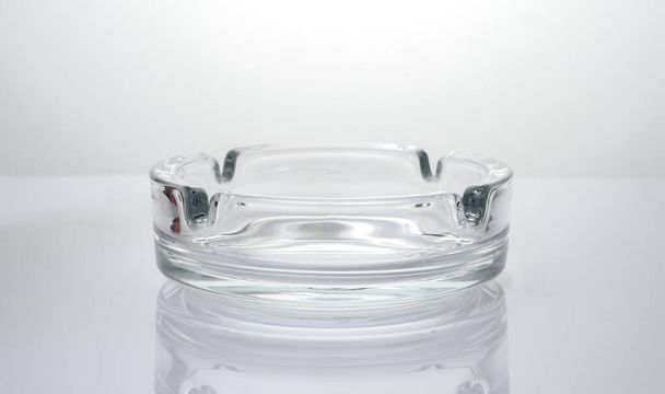 Transparenter Glas-Aschenbecher auf glänzend hellem Hintergrund. - Foto, Bild