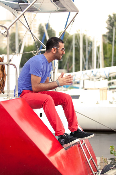 Latin férfi ül a fedélzeten a piros yacht kikötő a - Fotó, kép