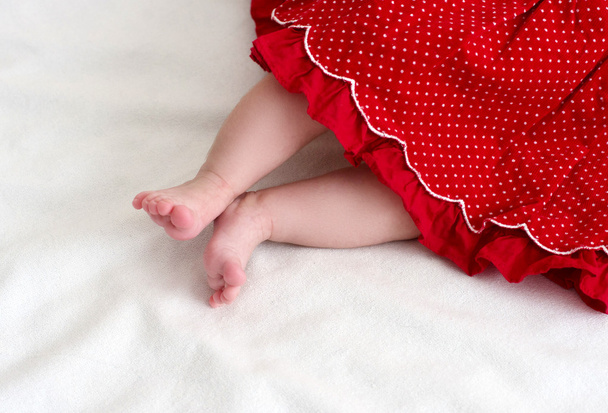 pasgeboren baby meisje voeten in rode jurk - Foto, afbeelding
