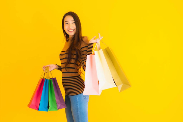 Retrato bonito jovem asiático mulher feliz sorriso com um monte de saco de compras a cores da loja de departamento no fundo isolado amarelo
 - Foto, Imagem