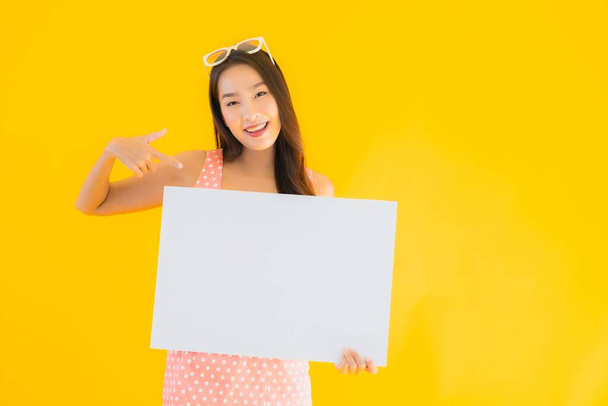 Portret piękna młoda azjatycka kobieta pokazać pusty biały billboard dla tekstu i copyspace na żółtym odizolowanym tle - Zdjęcie, obraz