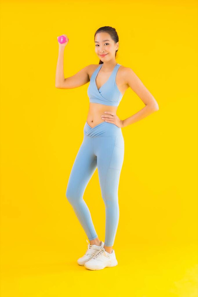 Retrato hermosa joven asiática mujer con mancuerna y ropa deportiva listo para el ejercicio en amarillo aislado fondo
 - Foto, imagen