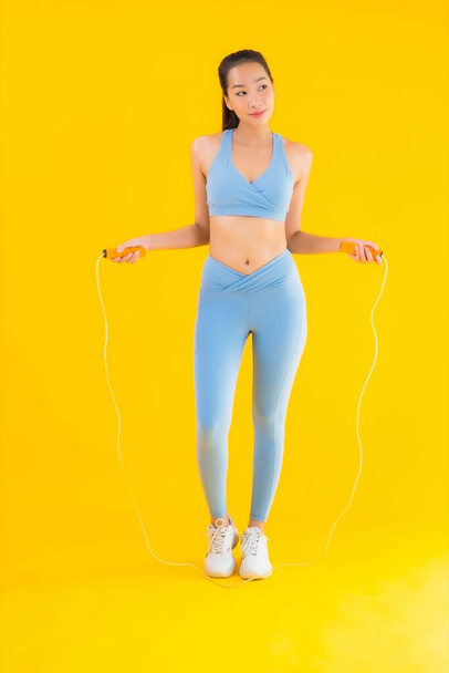 Portrait beautiful young asian woman wear sportwear with rope ready for exercise on yellow isolated background - 写真・画像