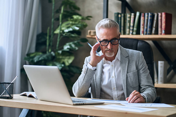 Adult businessman with beard thinking about solving problems looking at charts and documents while working in the office. Business concept - Foto, Bild