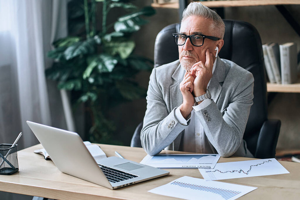 Adult businessman in stylish clothes sitting at his desk in the office while thinking about further tasks in work. Business career concept - Foto, Bild