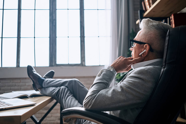 Back view photo of handsome adult businessman in glasses relaxing with legs on table while looking out the window. Business concept. Copy space - Foto, imagen