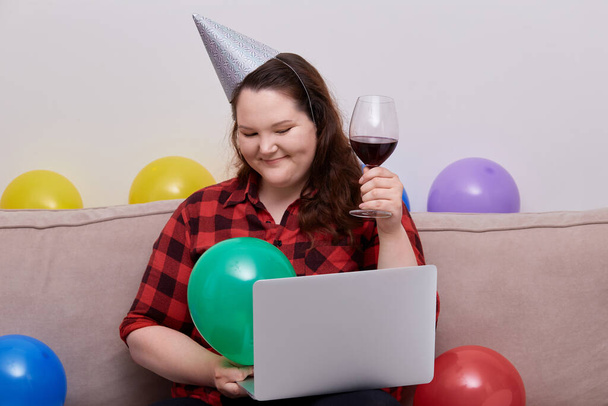 Μια μεγάλη γυναίκα γιορτάζει τα γενέθλιά της κατά τη διάρκεια της πανδημίας και πίνει κρασί.. - Φωτογραφία, εικόνα