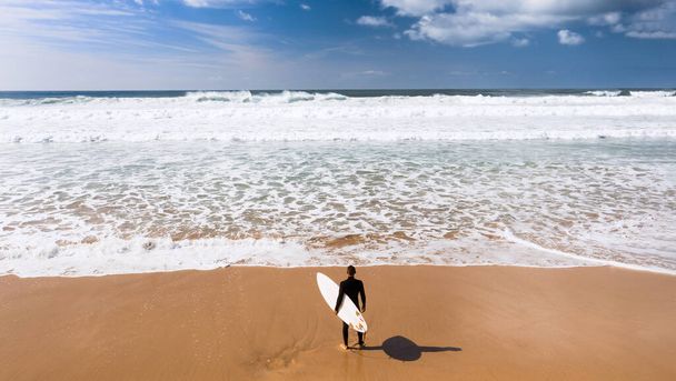 Horní pohled na muže surfaře v neoprénu s prknem stojící v blízkosti oceánu na písečné pláži.Připraven surfovat. Atlantický oceán, Portugalsko. Kvalitní fotografie - Fotografie, Obrázek