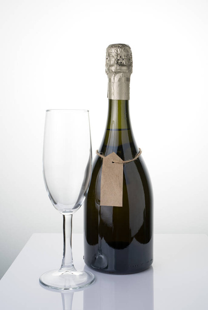 Una botella de alcohol con una etiqueta en una cuerda y un vaso sobre un fondo claro. - Foto, Imagen