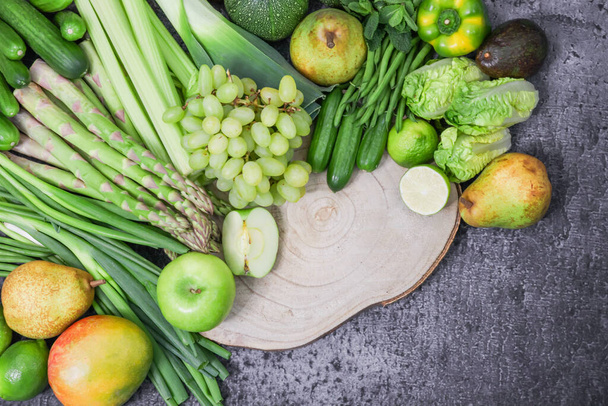 Green fruits and vegetables with a wooden board are arranged in a semicircle on the left with space for text on the right, a close-up top view. - 写真・画像