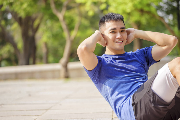 jeune homme formation et faire des redressements assis dans le parc - Photo, image