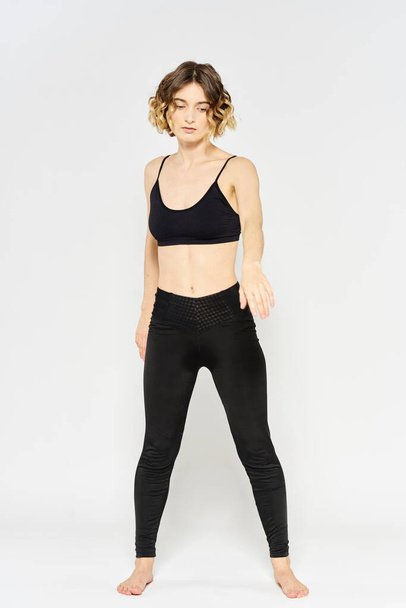femme sportive en jean noir et un t-shirt faisant des exercices dans une pièce lumineuse - Photo, image