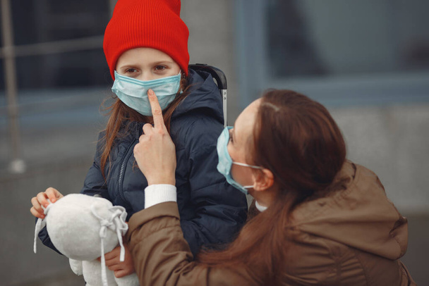 A European mother in a respirator with her daughter are standing near a building.The parent is teaching her child how to wear protective mask to save herself from virus - Photo, Image