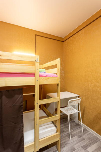 Wooden bunk bed with curtains, desk and chair in large hostel dorm room - Фото, изображение