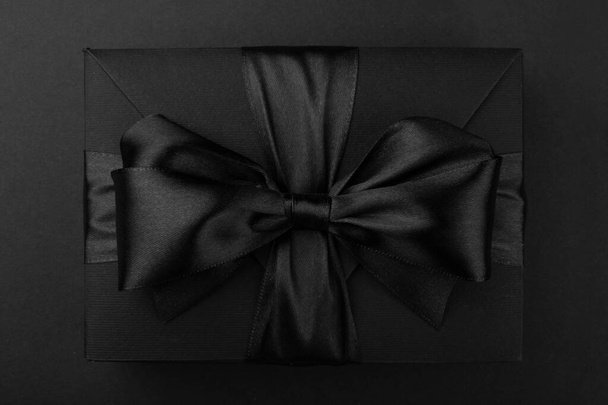 Zwarte vrijdag cadeau, papieren doos met zijden lint strik op zwarte papieren achtergrond met kopieerruimte voor tekst, platte lay top view sjabloon - Foto, afbeelding