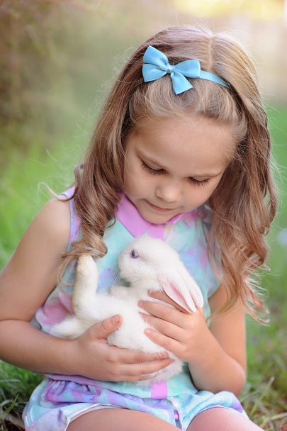 Cute little girl with a bunny rabbit has a easter at green grass - Фото, изображение