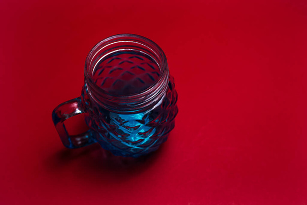 Gros plan de tasse en verre bleu pour jus sur fond sombre de couleur rouge. - Photo, image