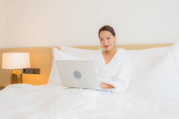Портрет красива молода азіатка використовує комп'ютерний ноутбук на ліжку в інтер'єрі спальні
 - Фото, зображення