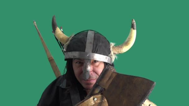 En cámara lenta. Fondo verde. Una flecha golpea el escudo de madera del guerrero vikingo. Hombre maduro en casco con cuernos y un hacha en las manos - Metraje, vídeo
