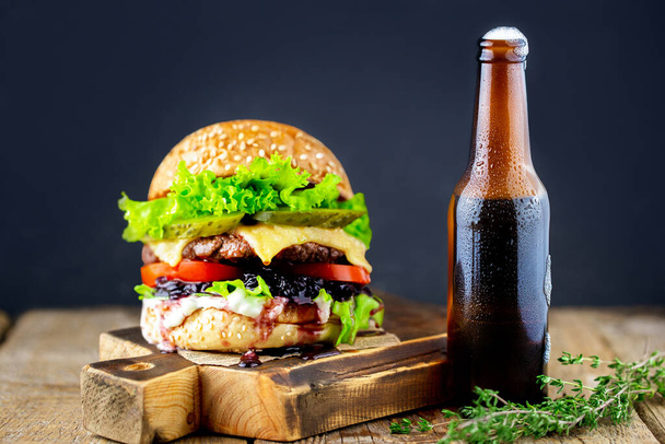 Big burger on a dark background.Beef burger. Delicious burger with sauce. Hamburger. Delicious grilled Angus burger with cheese, salad and tomatoes on a sesame bun. Fast food. Homemade hamburger - Фото, изображение