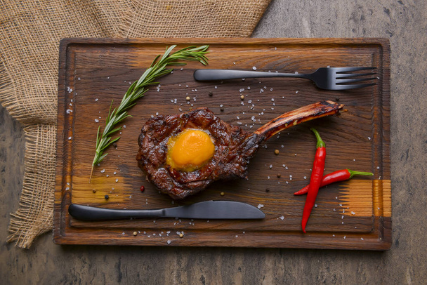Barbecue tomahawk steak with spices served on a rustic wooden board over wooden background. BBQ concept, grilled meat steak, autumn seasonal dish. - Fotó, kép