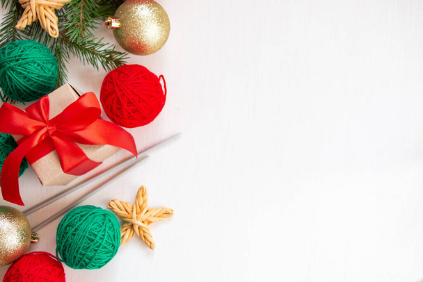 クリスマスの構図。糸の赤と緑のボール、白い背景に赤い弓を持つ贈り物。明るい糸編みの概念。フラットレイアウト、トップビュー. - 写真・画像