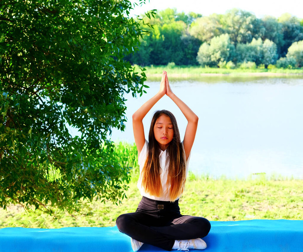 湖のそばの緑の公園でヨガの練習をしている若い女性。健康的なライフスタイルのコンセプト - 写真・画像