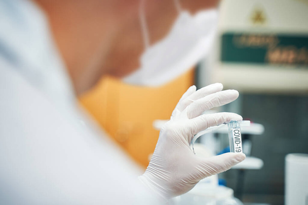 Lab worker holding a test tube with a coronavirus test substance, laboratory analysis, closeup - Foto, afbeelding