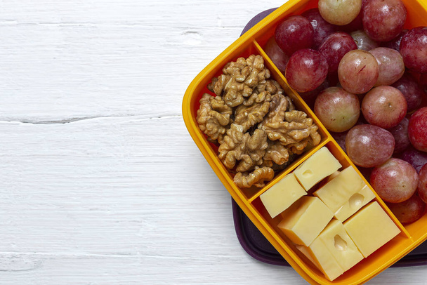 Comida saludable en recipientes de plástico listos para comer con queso, uvas y nueces en la mesa de trabajo. Para quitarse.nueces - Foto, Imagen