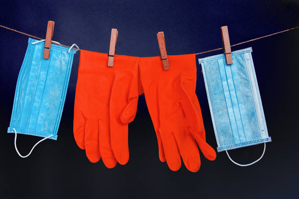  Latexhandschuhe und eine medizinische Gesichtsmaske hängen an Wäscheklammern auf grauem Hintergrund. Sicherheitskonzept während der Coronavirus-Pandemie. - Foto, Bild