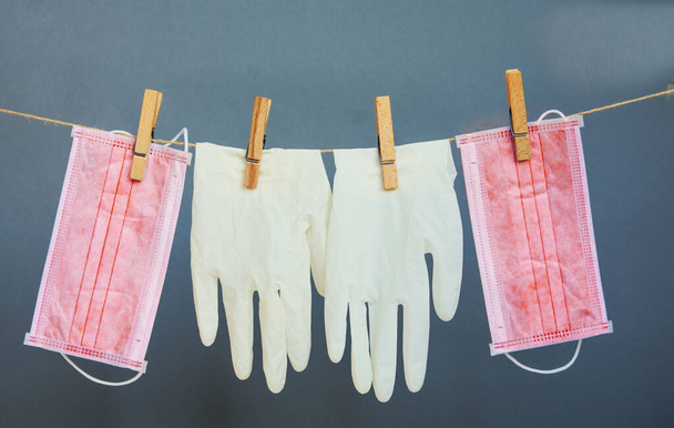  latex gloves and a medical face mask hang on clothespins on a gray background. safety concept during the coronavirus pandemic. - Foto, Bild