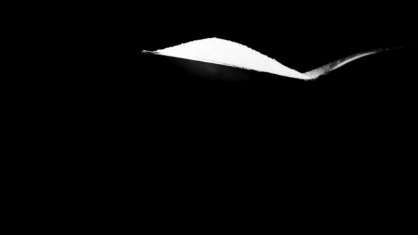 Azúcar blanco cayendo de la cuchara en cámara lenta aislado sobre fondo negro - Imágenes, Vídeo