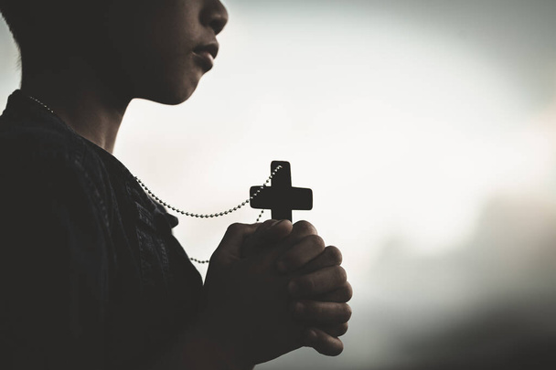 Αγόρι χέρια κρατώντας ένα ιερό σταυρό και προσεύχεται στο Θεό, παιδί προσεύχεται για το Θεό Θρησκεία. - Φωτογραφία, εικόνα