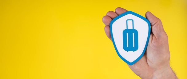 Концепция страхования багажа с бумажным щитом, держащимся рукой на желтом фоне - Фото, изображение