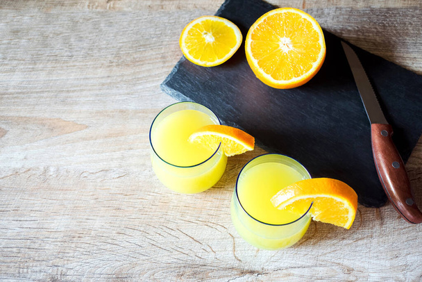 Orangensaft-Coctails in Gläsern, frisch geschnittenes Obst auf Schneidetisch mit Messer, Holzhintergrund. - Foto, Bild