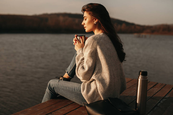 Calm woman with cup of hot drink sitting near lake - Foto, Imagen