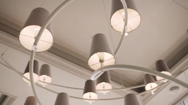 Un grand lustre blanc élégant se compose d'un long tube torsadé et d'un grand nombre d'ampoules avec des abat-jour au plafond dans un restaurant cher. - Séquence, vidéo