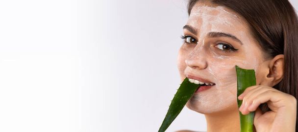 Banner- long format. Brunette girl with cream on her face and long healthy hair. Holding a broken scarlet leaf in my teeth Photo over white background with empty side space. High quality photo - 写真・画像