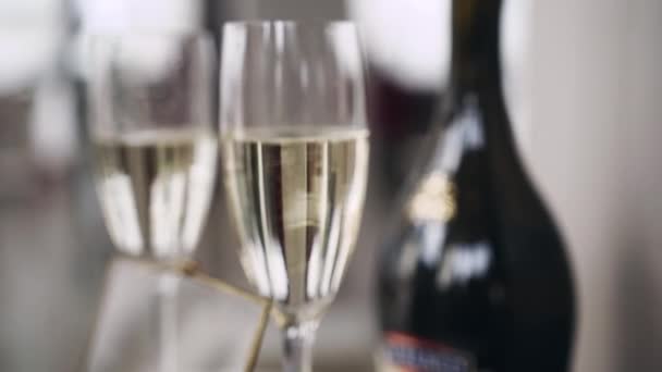 Bubbles of white champagne that rise quickly in a clean transparent half-filled tall glass against the background of a blurred second glass and a bottle of champagne. Action shot - Footage, Video