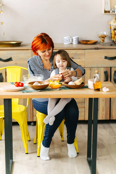 Cook together at home. Red-haired grandmother and little granddaughter cook pizza in a cozy home. Have fun in the kitchen - Фото, зображення