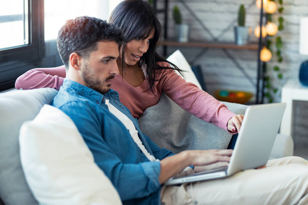 Shot of confident beautiful couple using computer while sitting on the couch at home. - 写真・画像