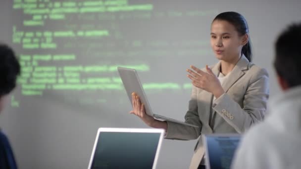 Gros plan moyen d'une étudiante métisse tenant un ordinateur portable dans les mains faisant rapport sur le codage du programme à ses camarades de classe dans une planche équipée moderne - Séquence, vidéo