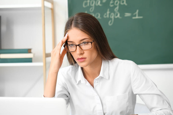 Stressed young female teacher in classroom - Foto, afbeelding
