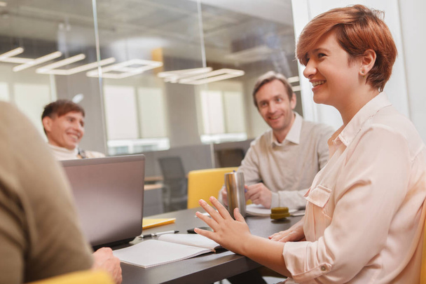 Female entrepreneur laughing, talking to her creative team during meeting at the office - Фото, изображение