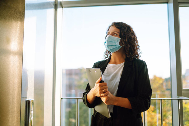 Portrait of businesswoman in protective face mask during virus epidemic while standing near elevator at modern office. Office manager back at work in office after quarantine. Covid-19. - Foto, immagini