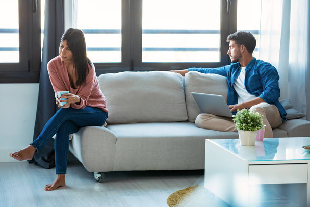 Shot of angry young couple sitting on couch together and looking to opposite sides at home. - Foto, Bild