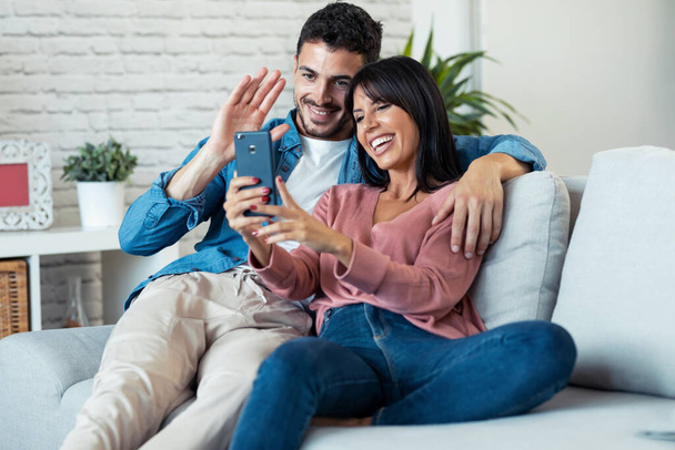 Shot of happy young couple making a video call with smart phone while sitting on couch at home. - Foto, afbeelding